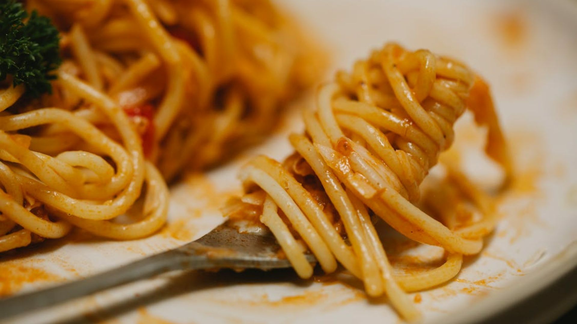 Pasta with tomato sauce and herbs served on a plate and twirled on a fork