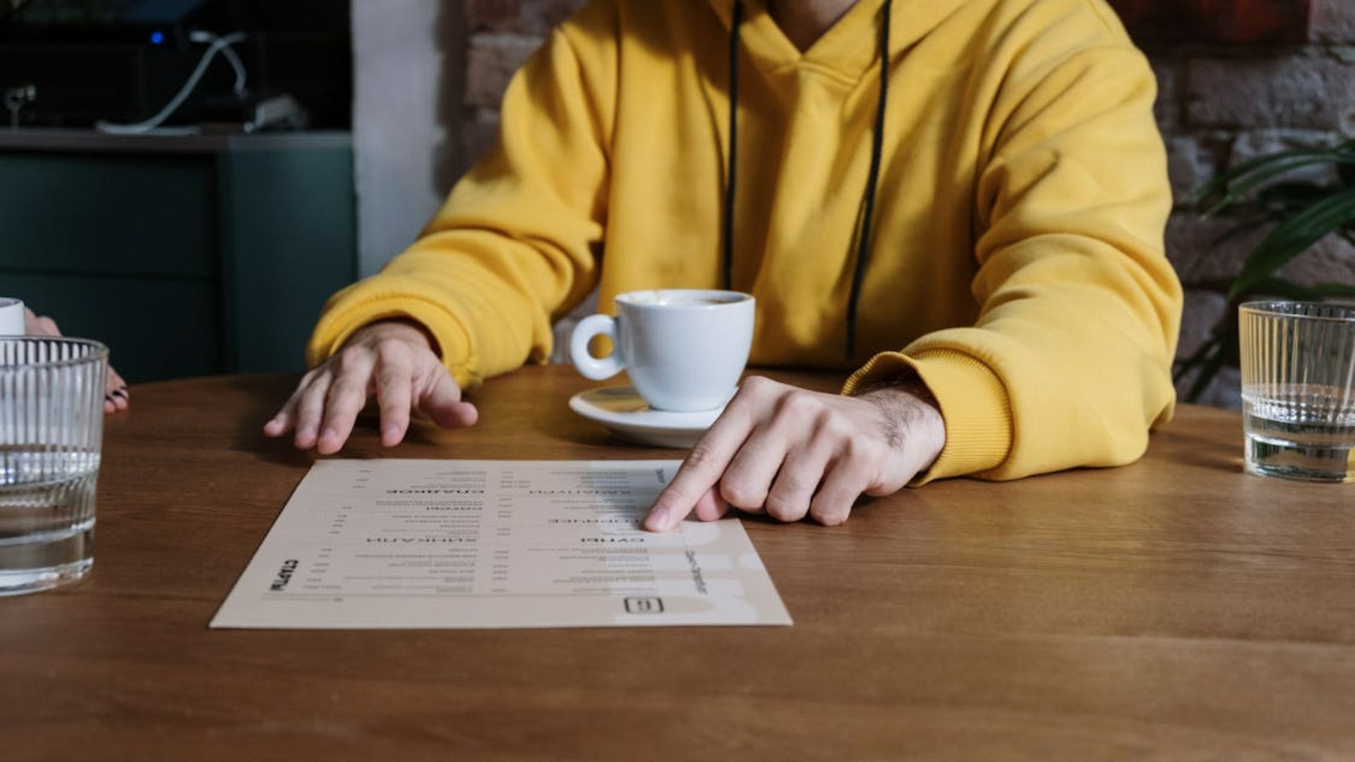 A man in a yellow hoodie pointing at a menu