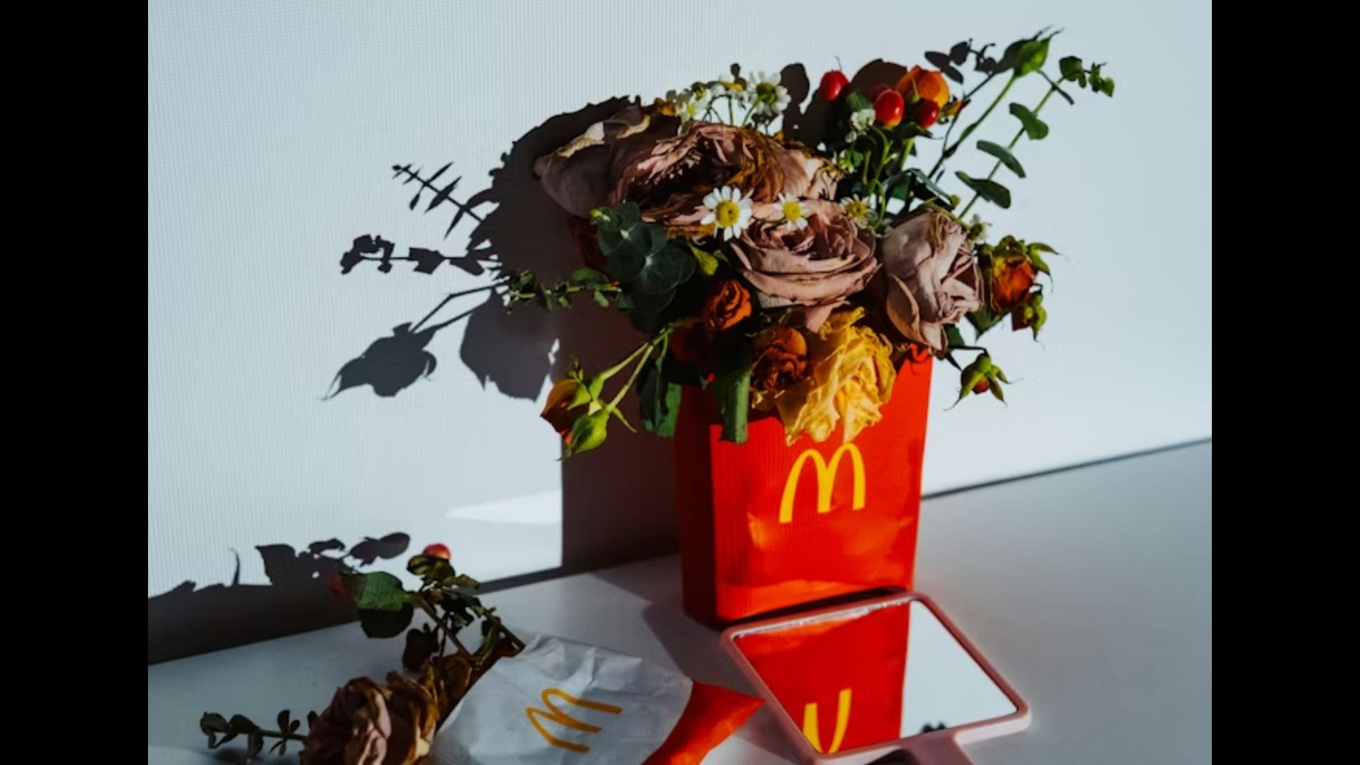 A McDonald’s red fries box and a regular fries container on the side used as a vase holding a floral arrangement