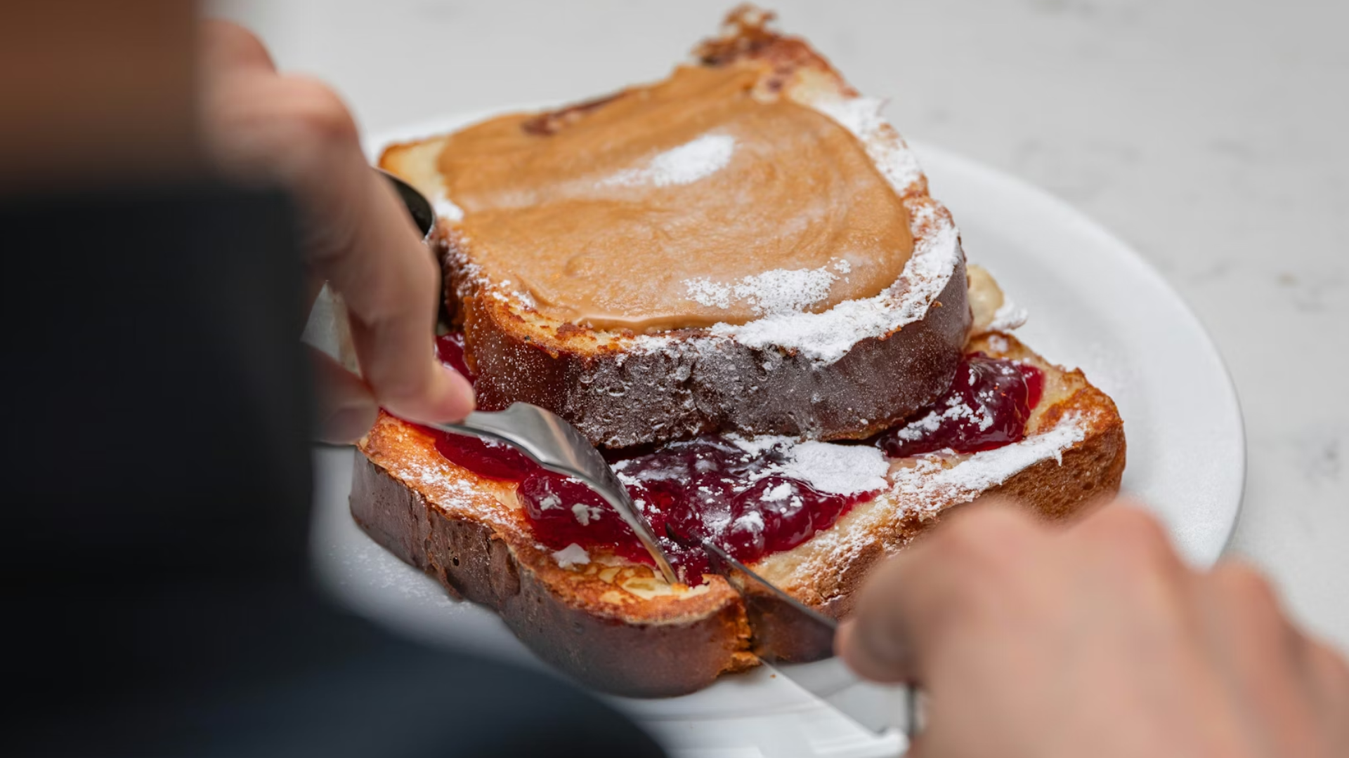 A Person Cutting To Their Peanut Butter Jelly on a Plate