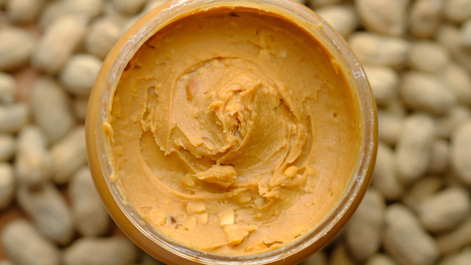 Close Up on Peanut Butter Jar with Peanuts on the Background