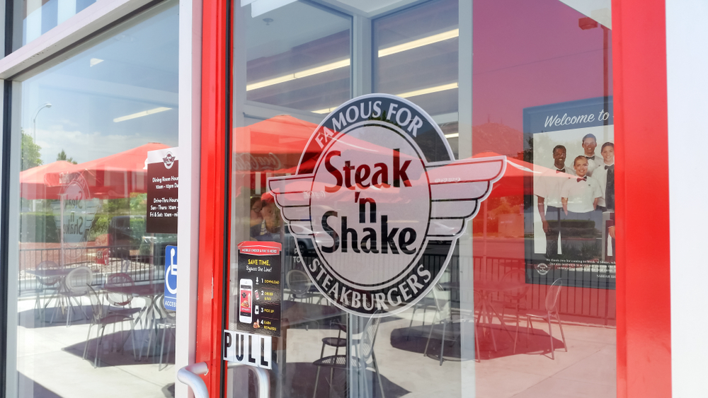 Steak ’n Shake logo on glass front door with outdoor patio seating visible through entrance.