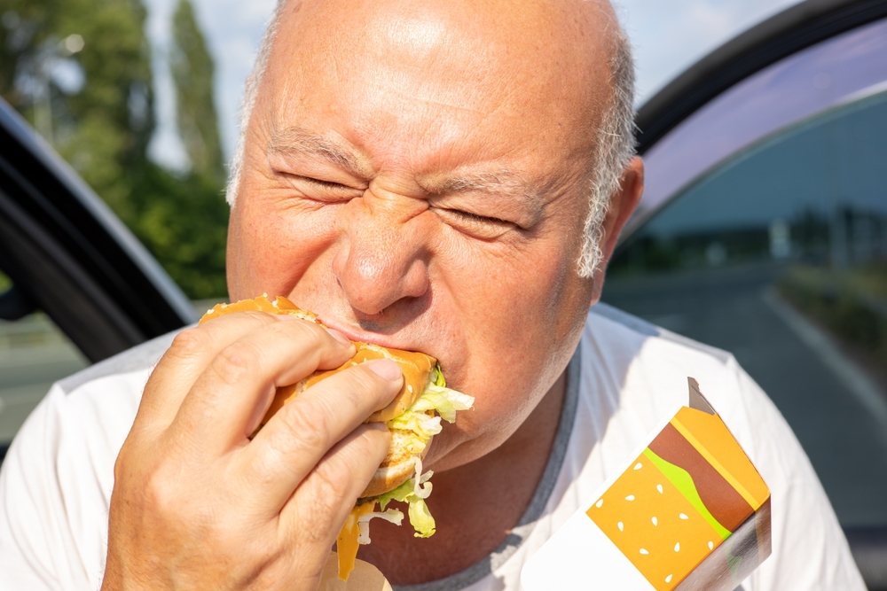 Elderly man taking a huge bite of a McDonald's burger.