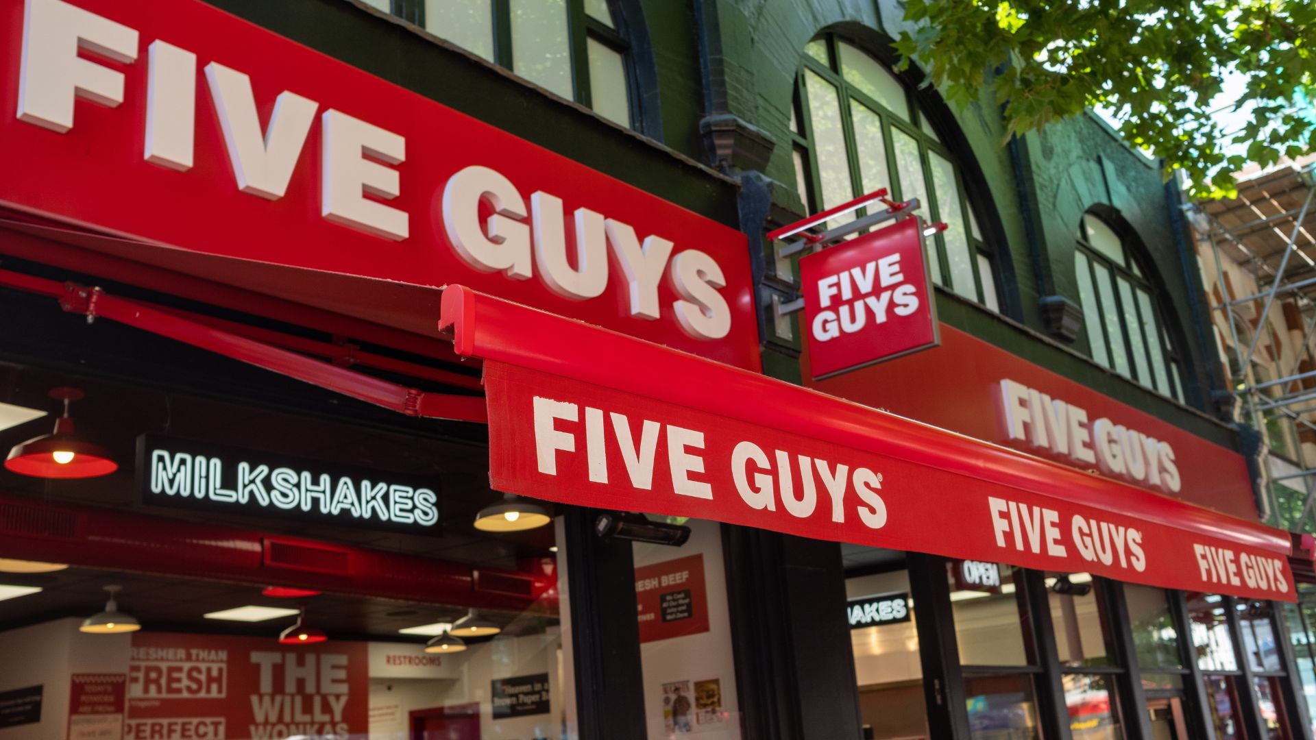 Five Guys restaurant storefront with red signage and awning on a city street.