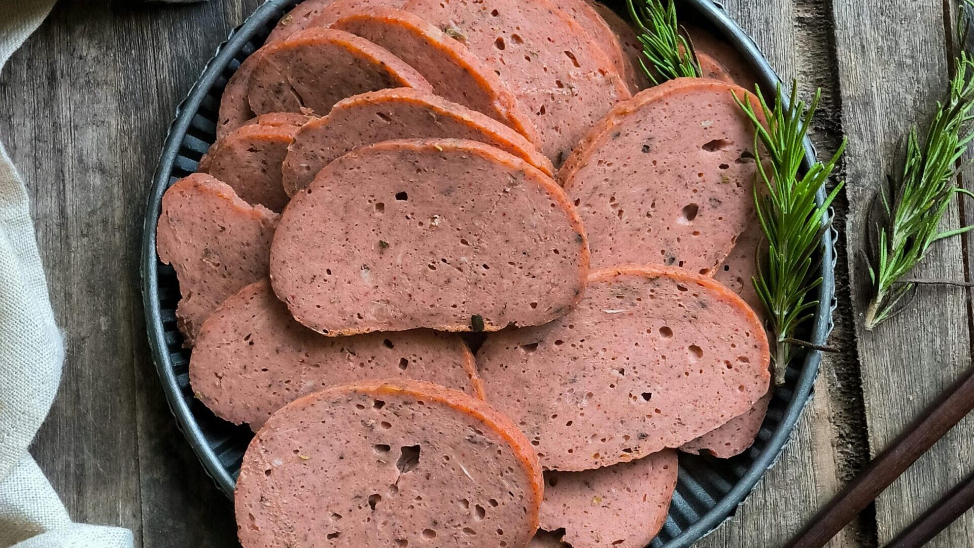 Slices of processed deli meat arranged on a plate with herbs.