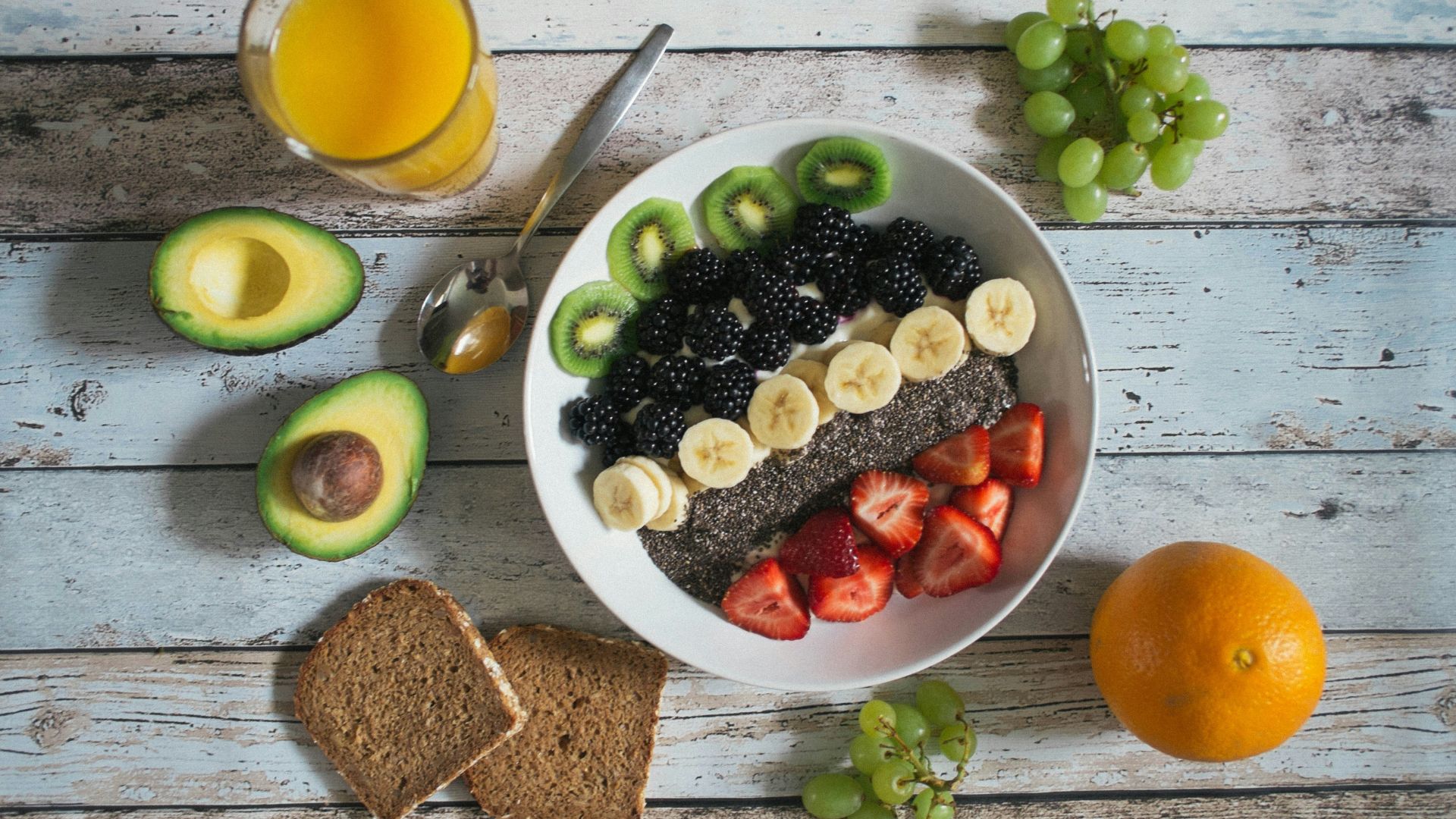 Bowl filled with fruit, seeds, and yogurt placed beside whole foods like avocado and bread