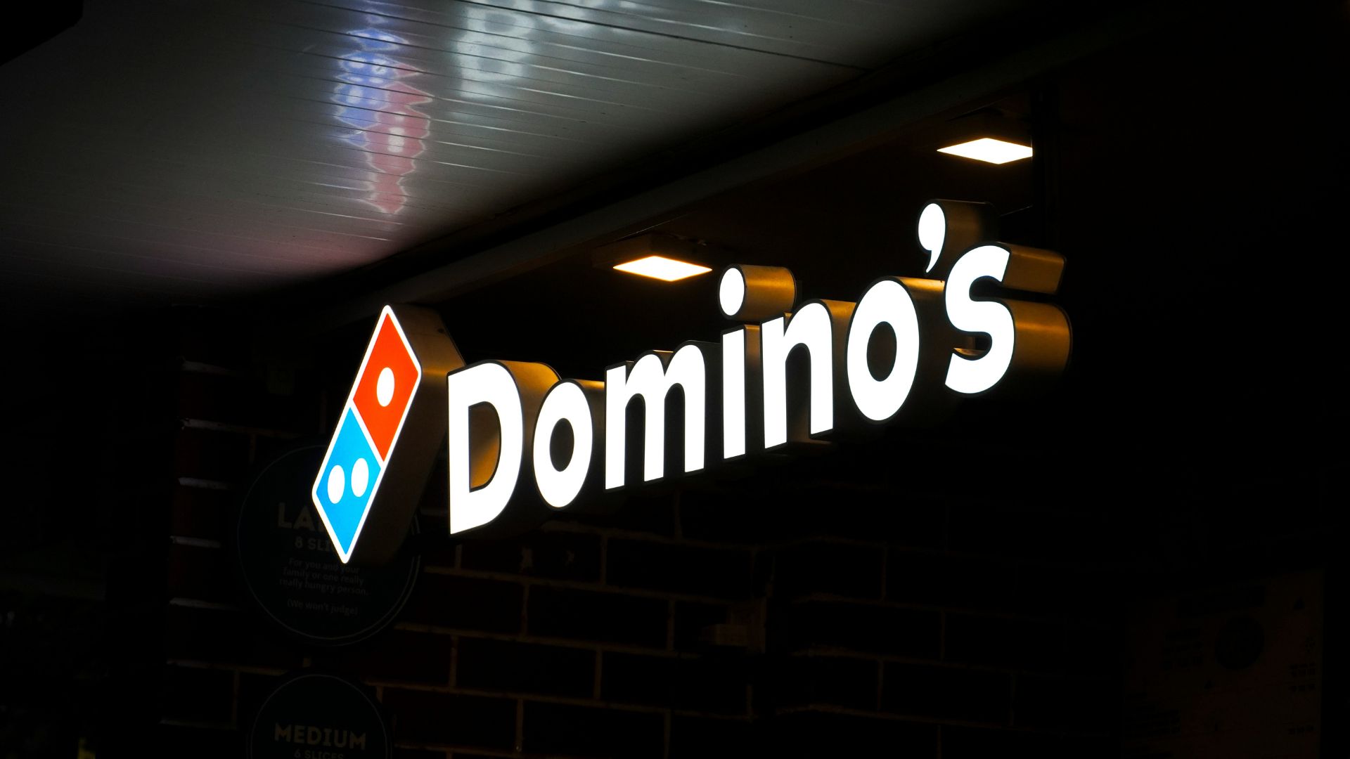 Illuminated Domino’s Pizza storefront sign glowing at night outside a restaurant