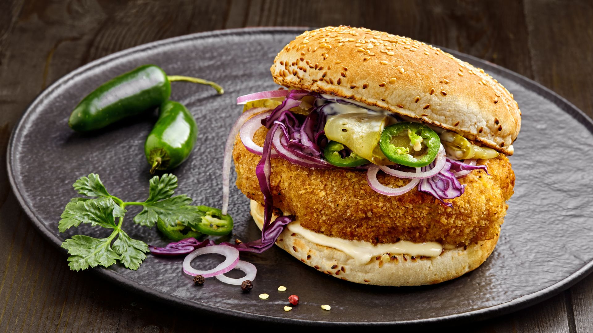 Crispy chicken sandwich with jalapeños, onions, and sauce on sesame bun.