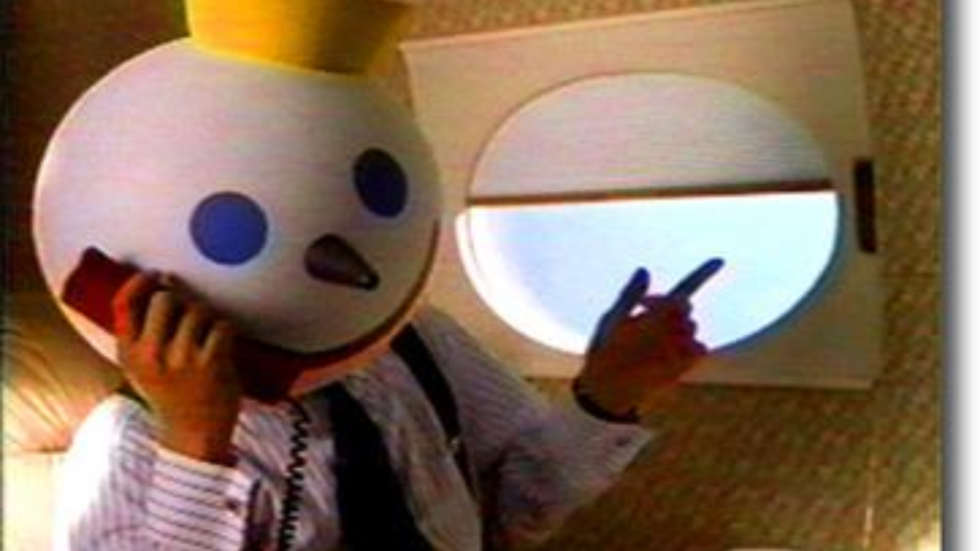 The Jack in the Box mascot, wearing a business suit and tie, talking on a red landline telephone while pointing out of an airplane window.
