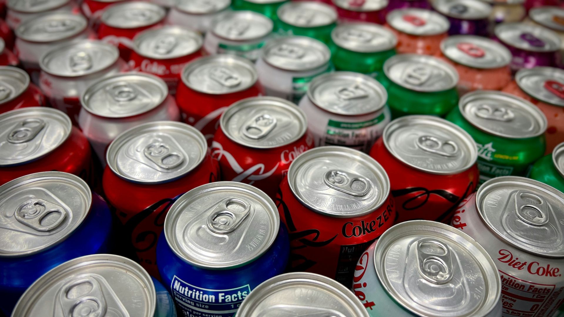Assorted soda cans including Coca-Cola, Diet Coke, and Sprite arranged together in a close-up view.