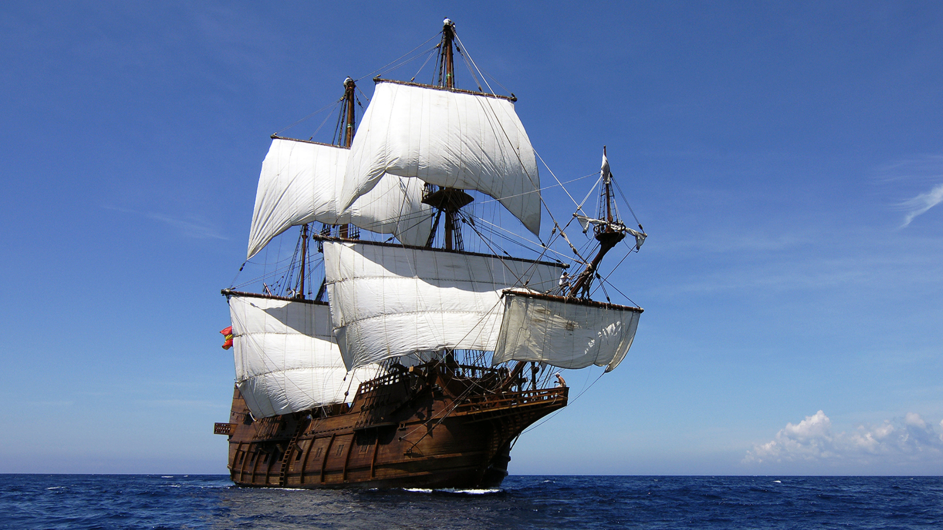 A majestic wooden galleon with large white sails fully unfurled, sailing across a deep blue ocean under a clear sky.