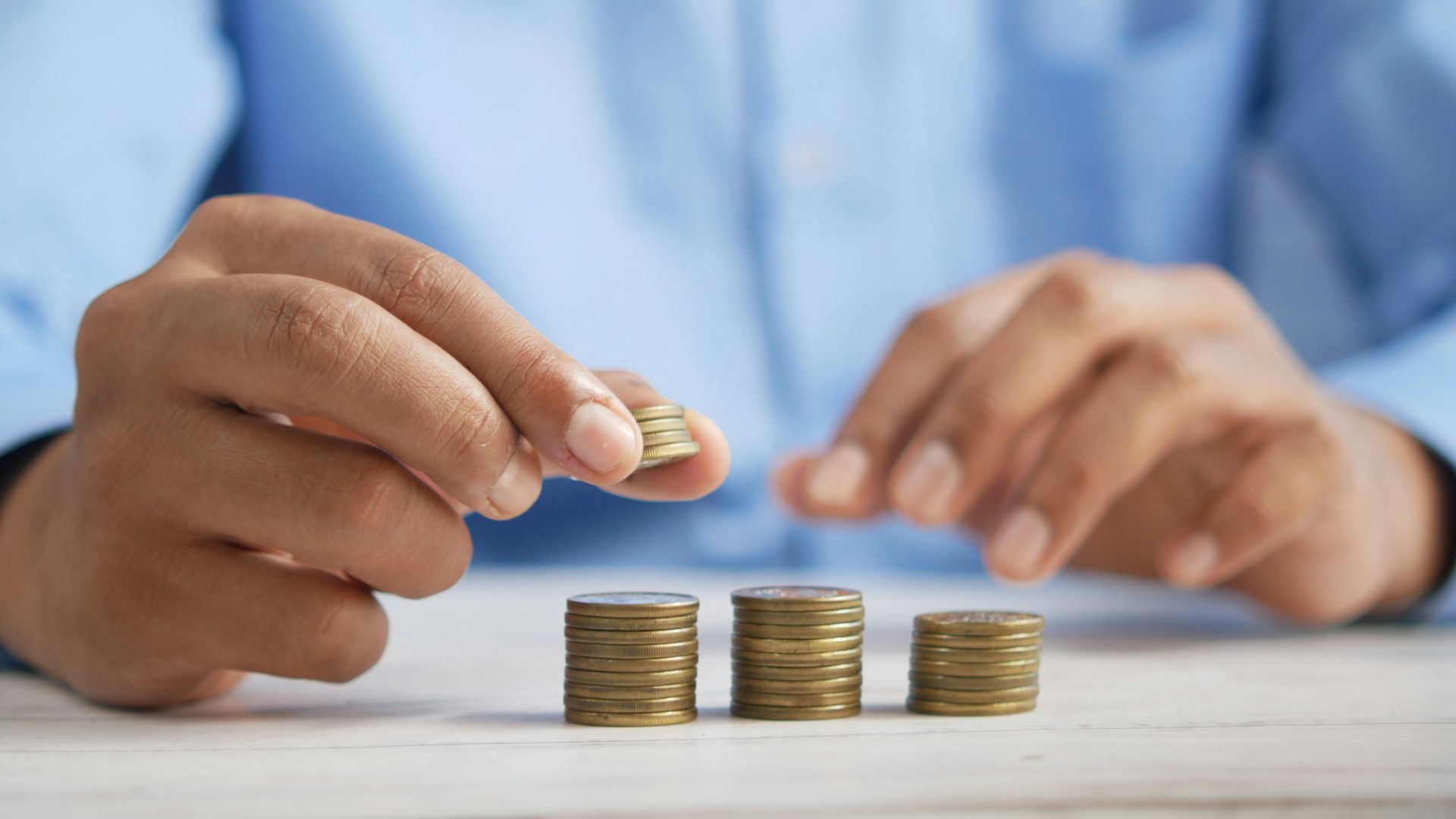 Person stacking small piles of coins on a table.