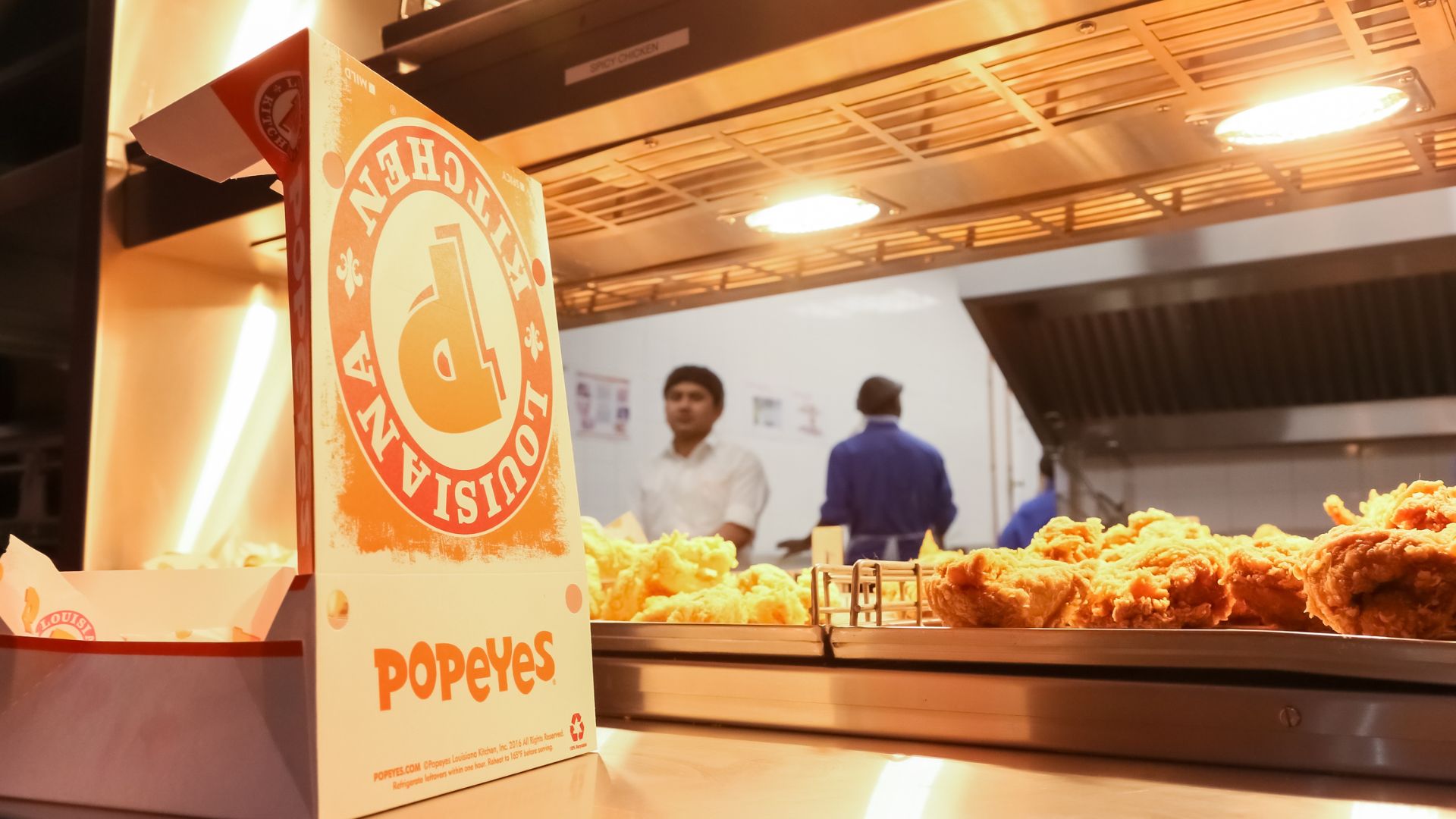 Popeyes fried chicken pieces displayed under heat lamps in a restaurant kitchen.