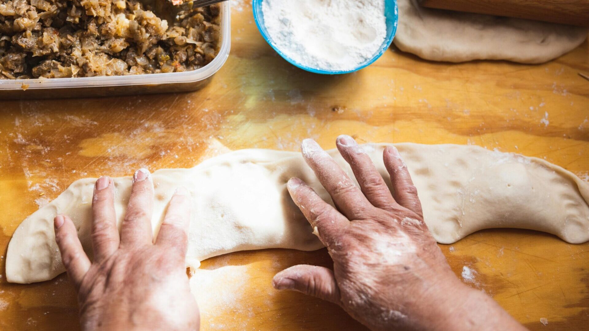 Person pressing and shaping dough by hand during food preparation.