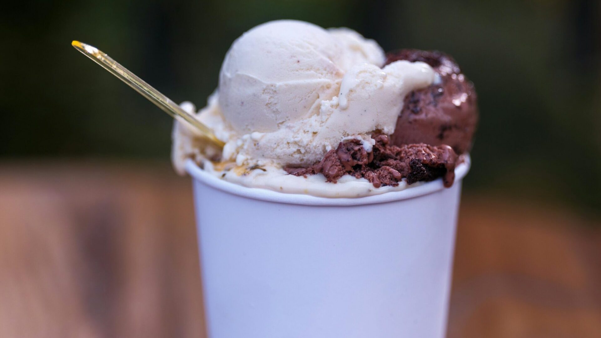 Cup of ice cream with multiple scoops and a spoon on a wooden table.