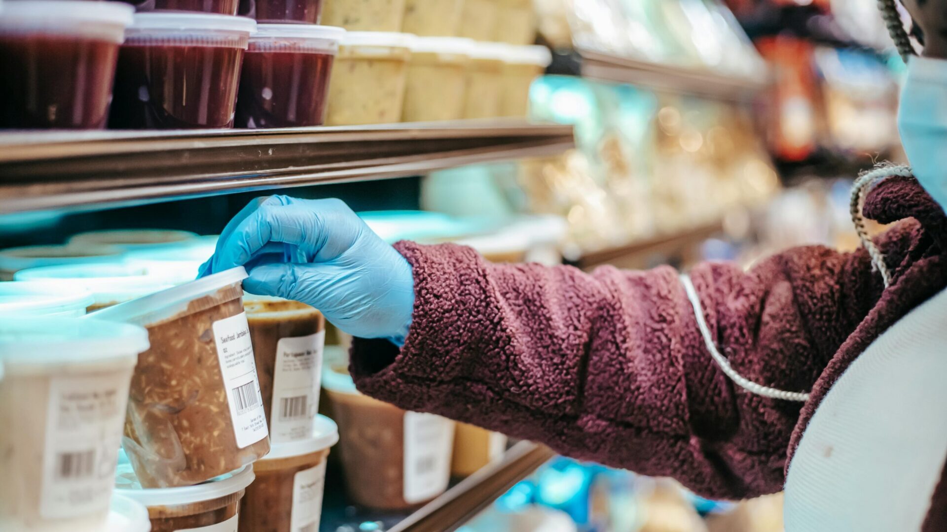 Gloved hand selecting packaged food items from a refrigerated store display.