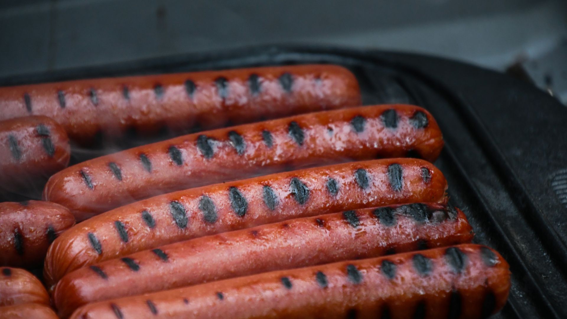 Beef hot dogs cooking on a grill with visible grill marks