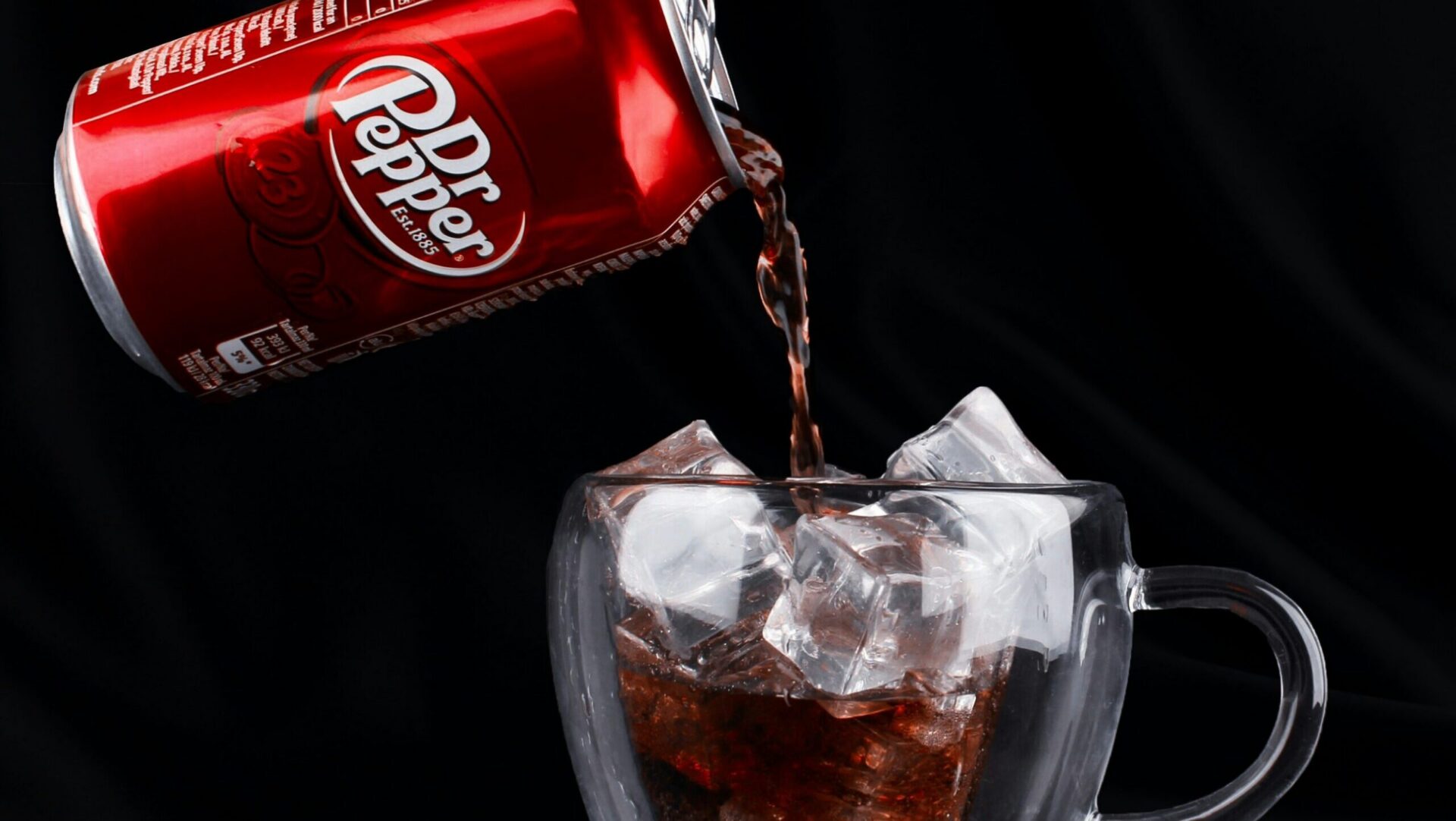 Dr. Pepper being poured from a can into a glass with ice.