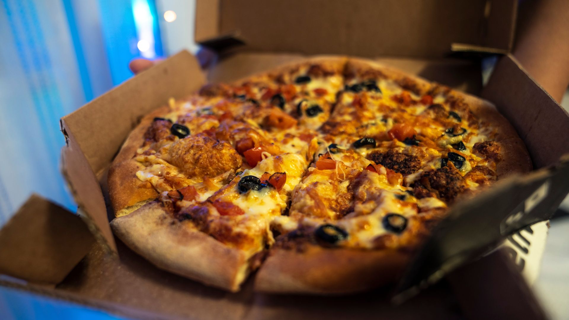 Fresh Domino’s pizza in a cardboard delivery box topped with olives, sausage, and vegetables