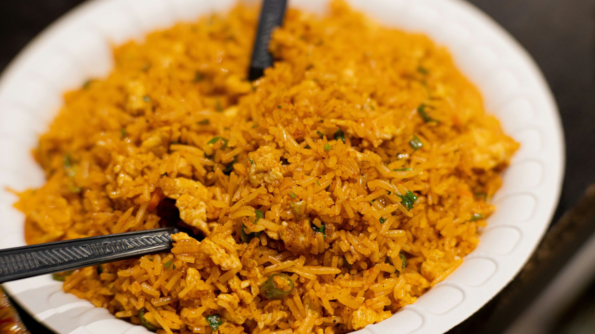 Bowl of cooked fried rice with eggs and vegetables served with black spoons on a white plate