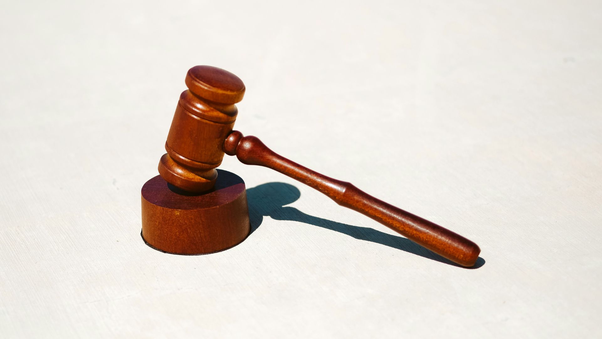 Wooden judge’s gavel resting on a sound block on a white surface.