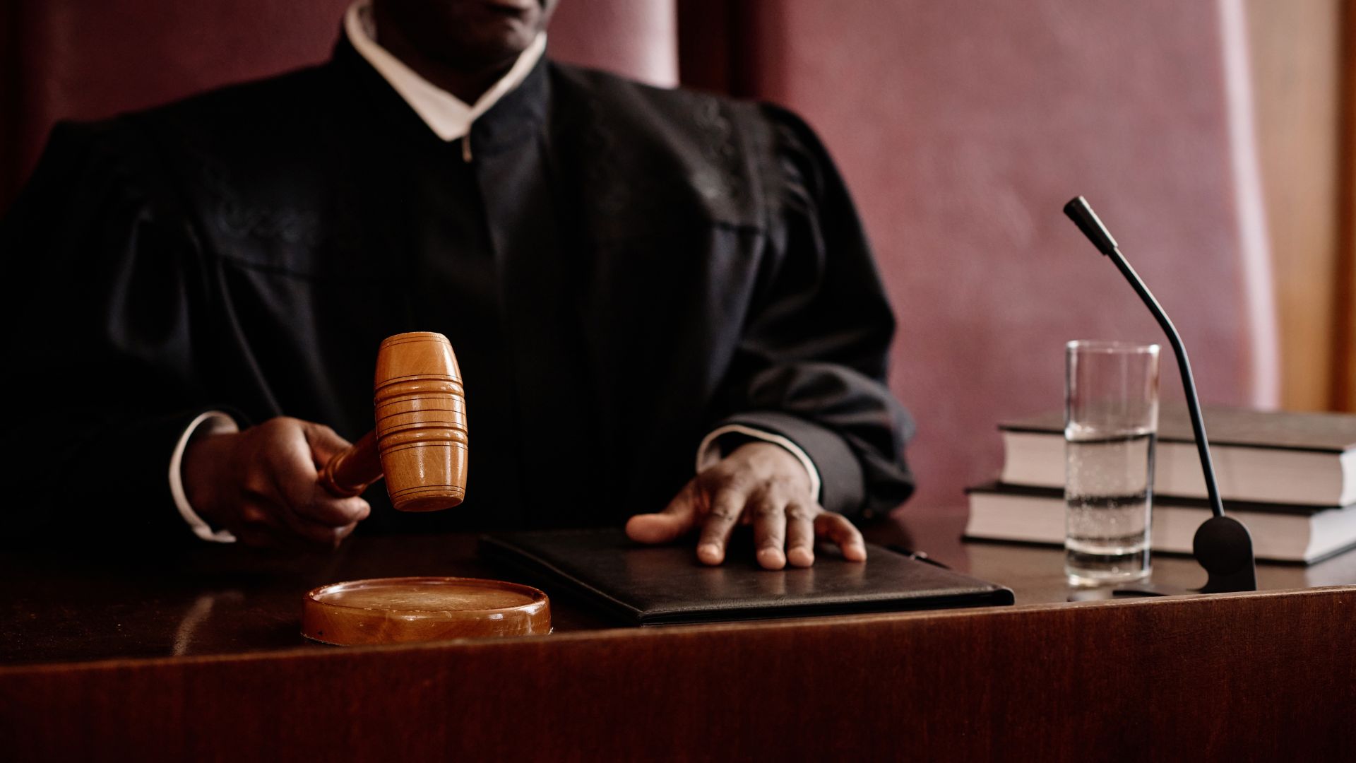 Judge holding a gavel over a desk in a courtroom during legal proceedings.
