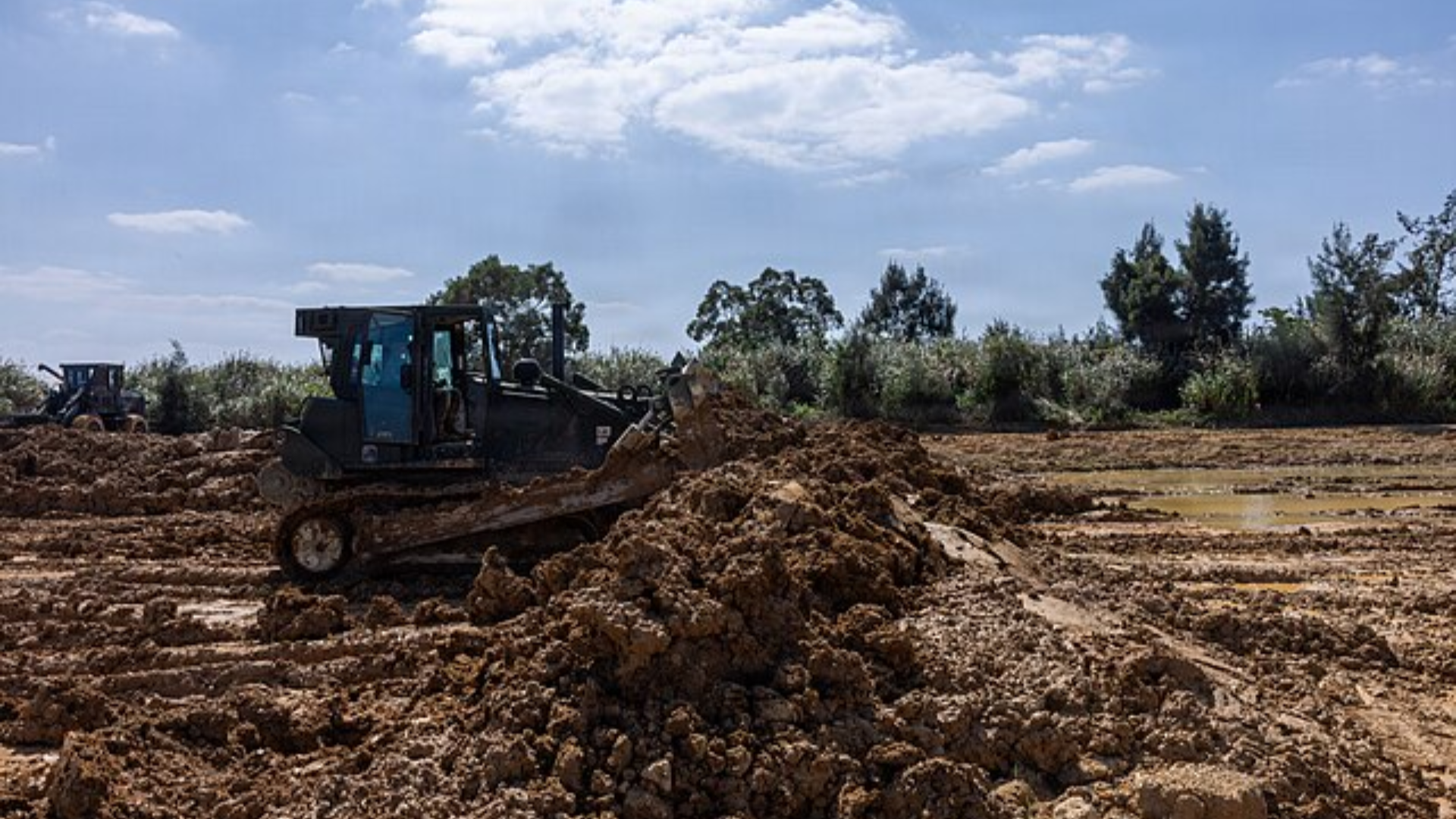 A large black bulldozer moving heavy mounds of brown dirt.