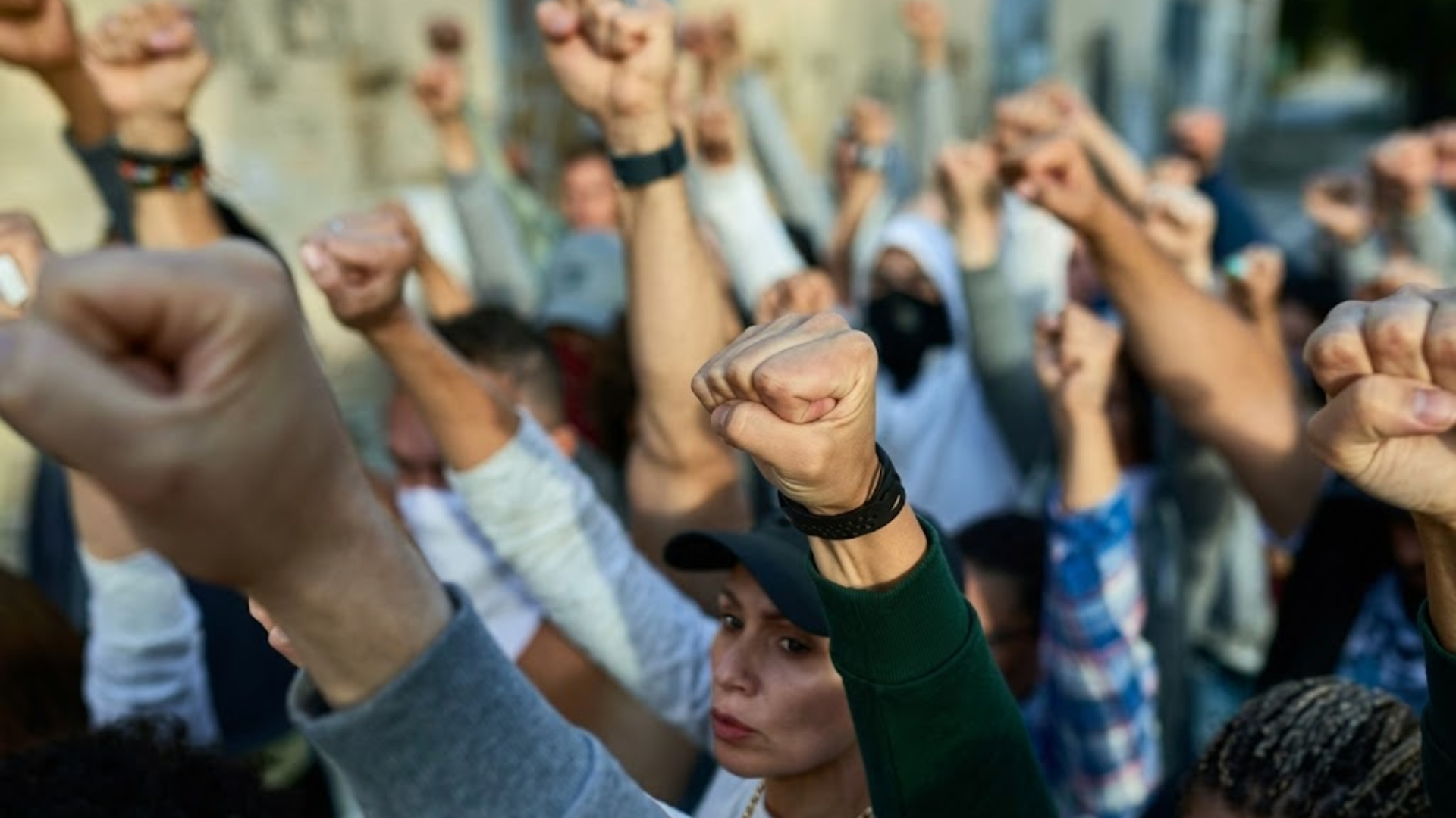 A group of diverse protesters standing close together and raising their clenched fists in the air during a protest.