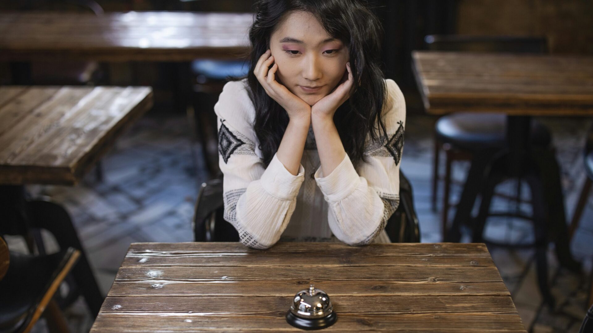 Woman resting her chin on her hands while waiting at a table with a service bell.