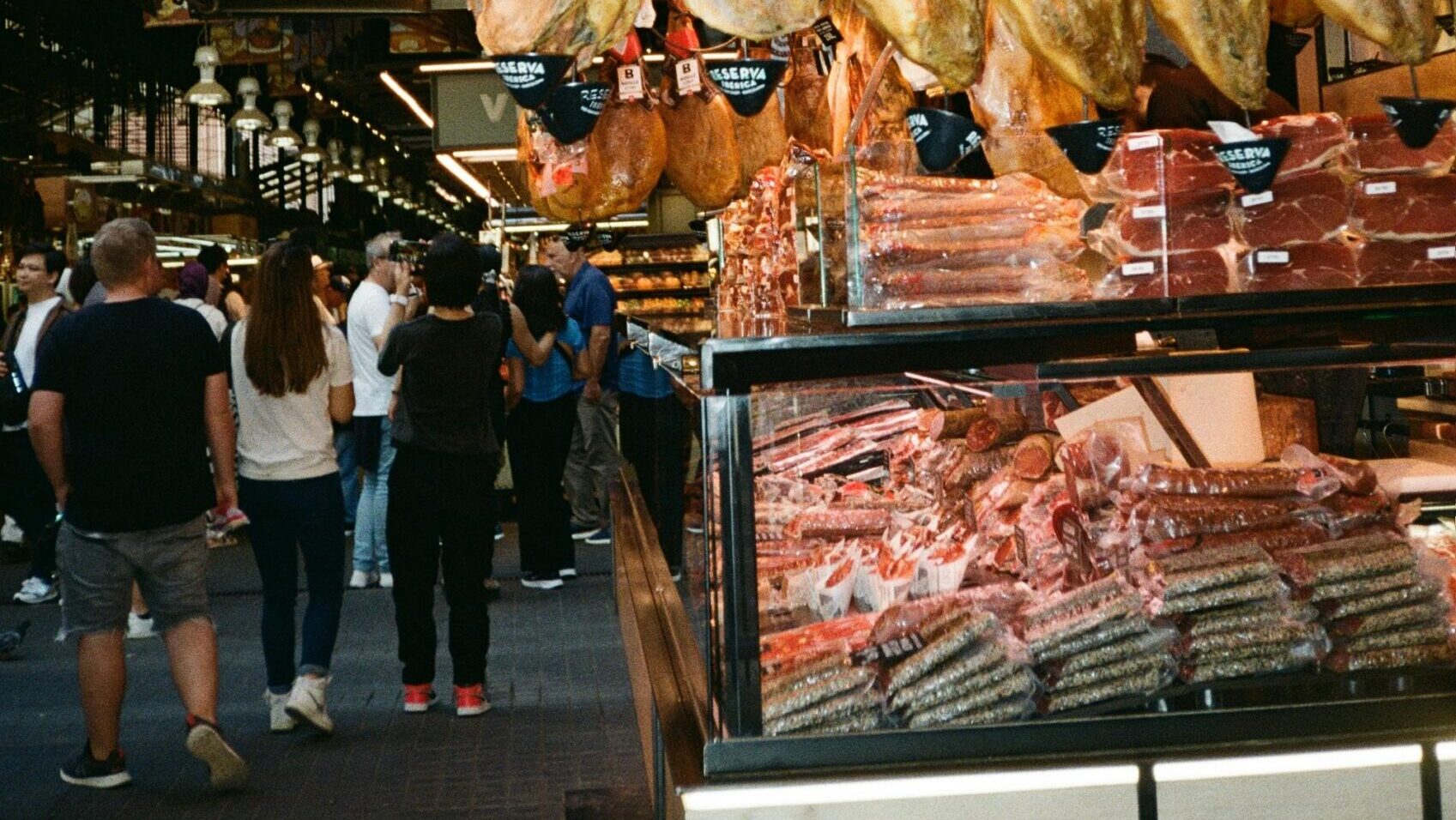 Cured meats hanging inside a deli section of a busy grocery store.