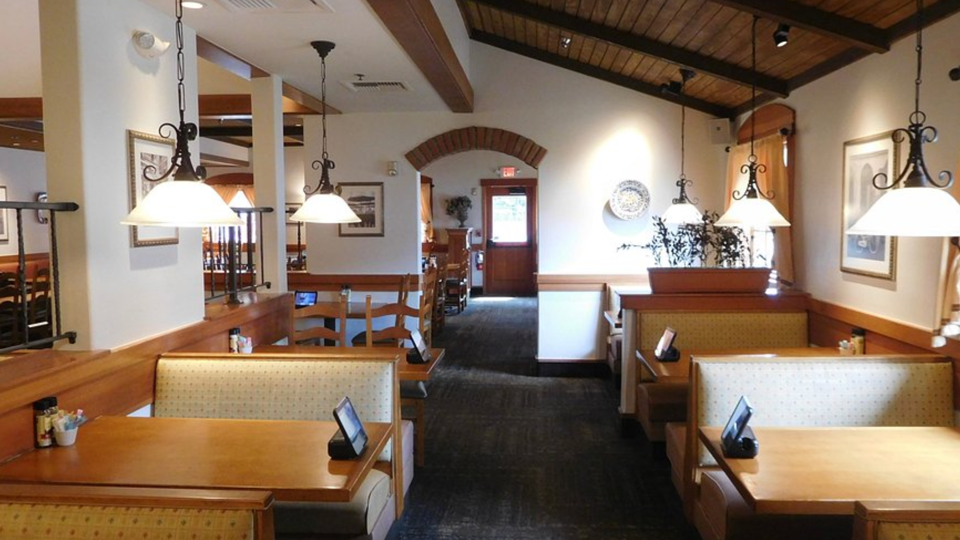 Interior view of an empty Olive Garden dining room featuring wooden tables, booths, and hanging light fixtures.