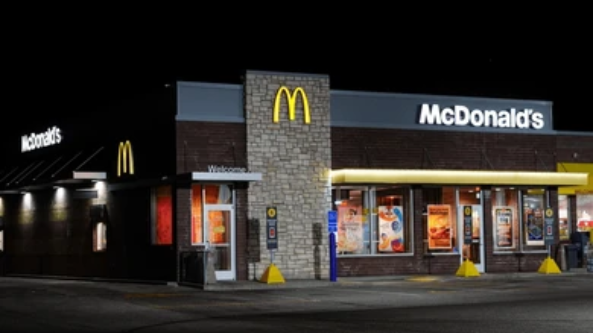 The exterior of a modern McDonald's restaurant at night, showing the illuminated golden arches and "McDonald's" signs against a dark sky.