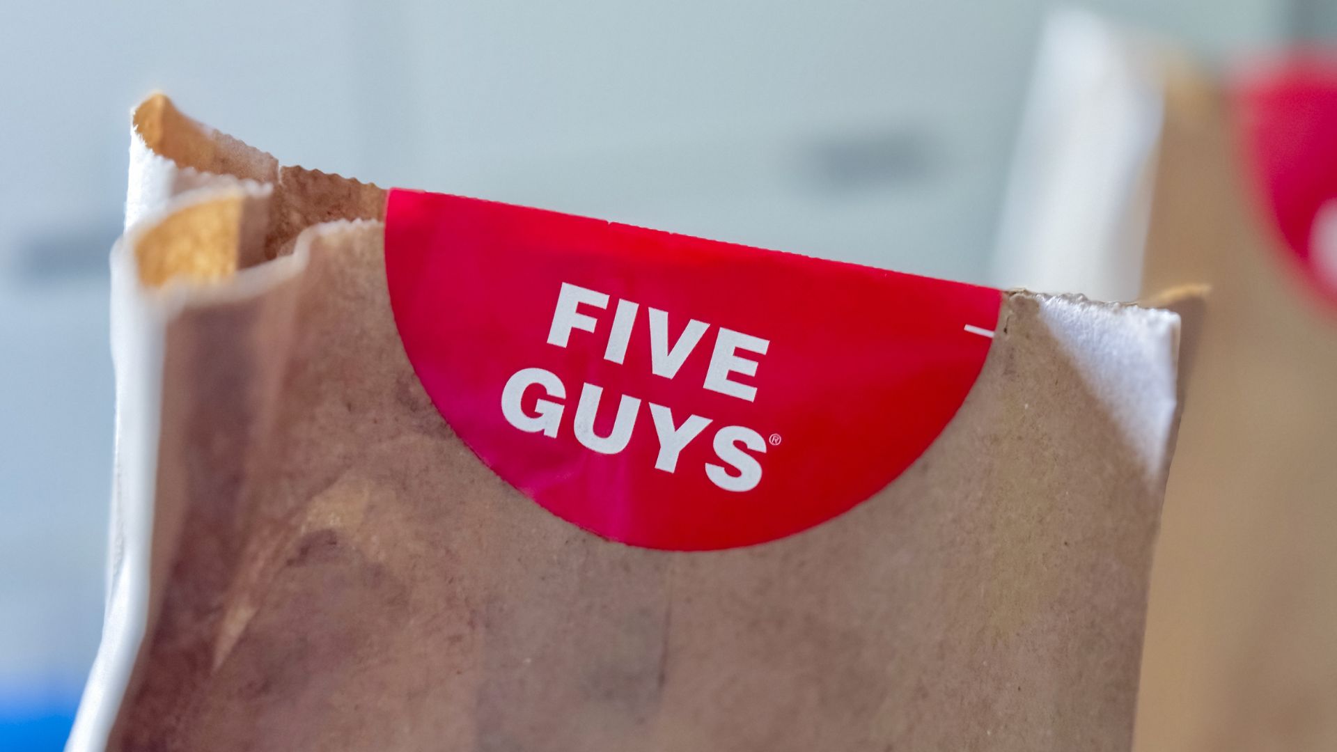 Five Guys takeout paper bag with red brand logo sticker on the front.