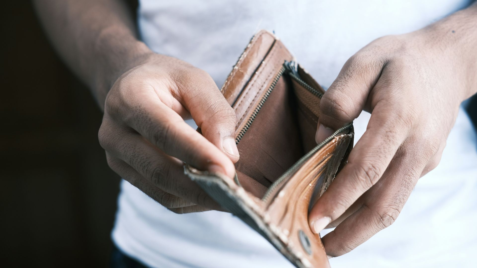 Person holding open a brown wallet showing no cash inside.