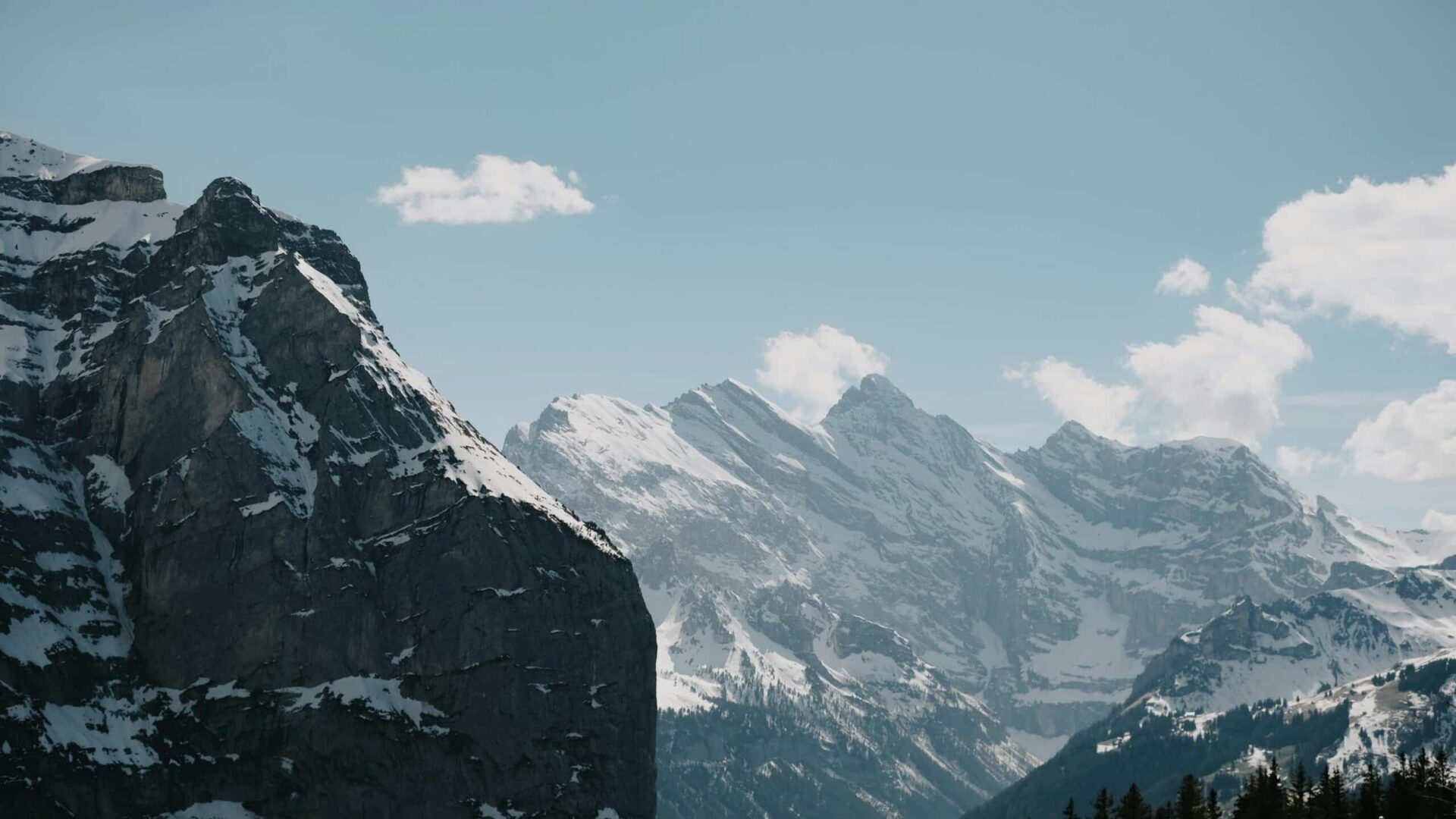 Snowcapped rocky mountains rising above a rugged landscape under a cloudy sky.