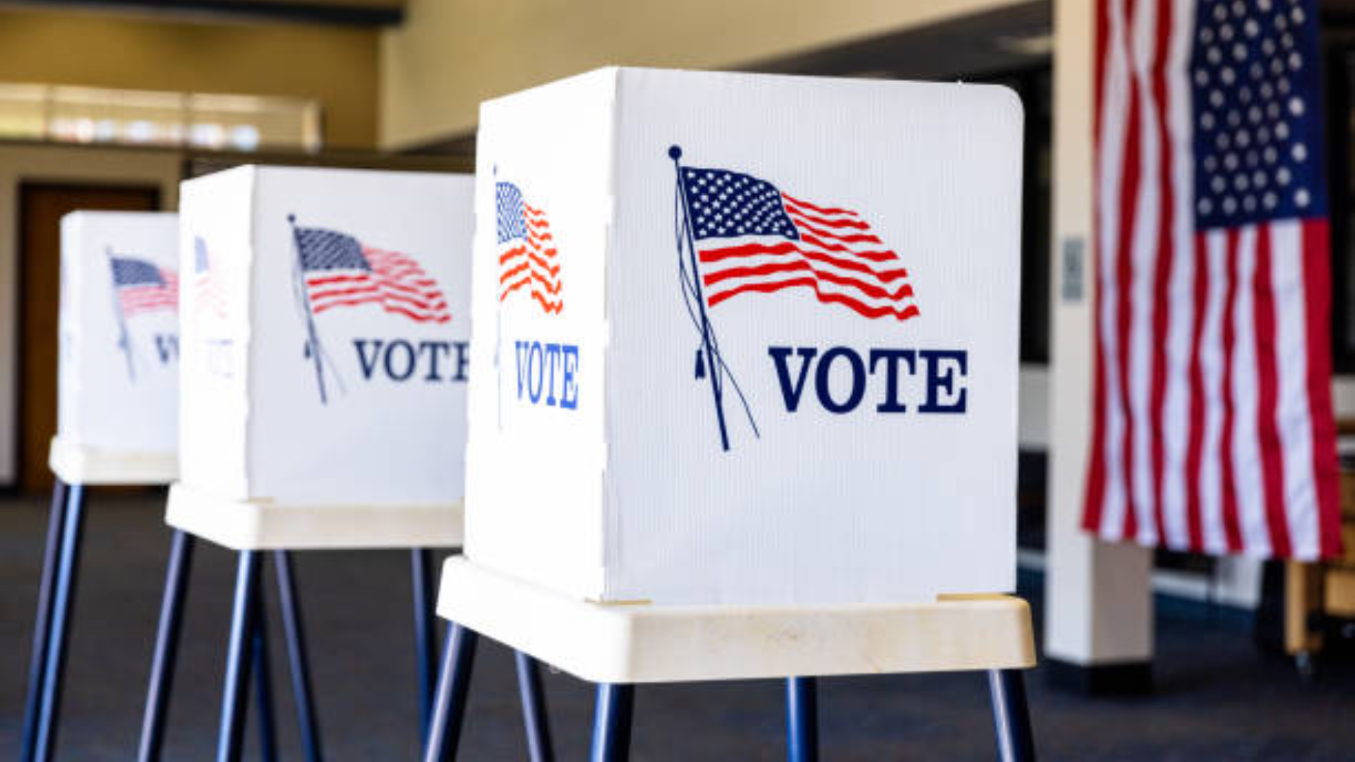 A row of white privacy voting booths featuring the American flag and the word "VOTE" at a polling station.