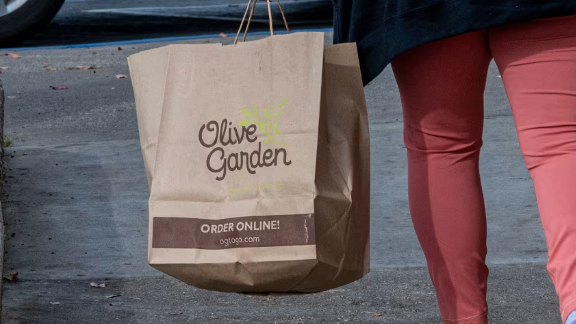 A person carrying a brown paper Olive Garden takeout bag.