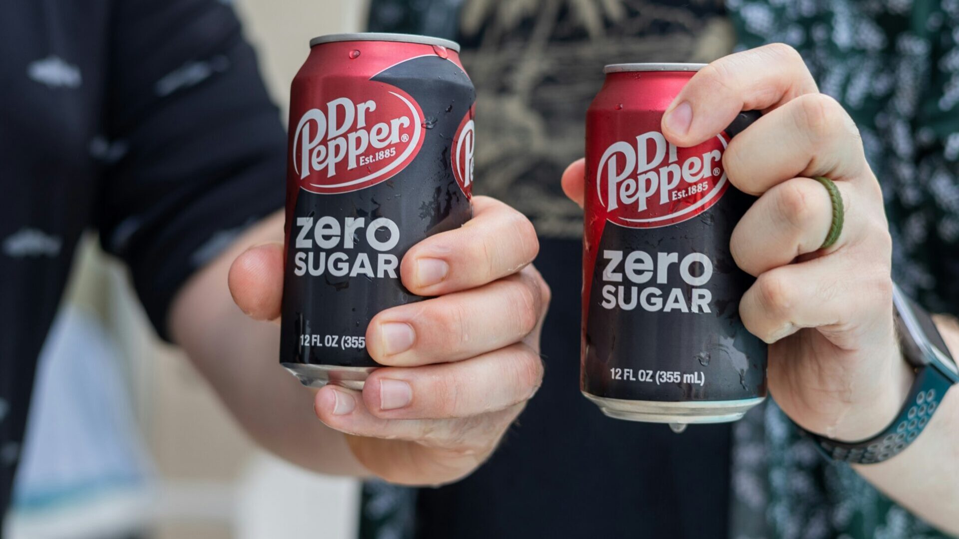 Two people holding cans of Dr Pepper Zero Sugar.