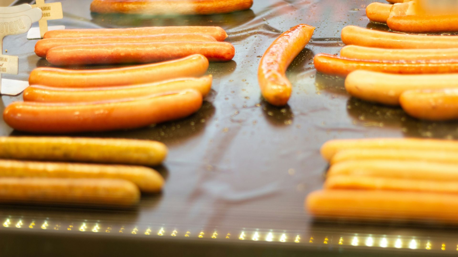 Several hot dogs heating on a grill often labeled uncured in packaging