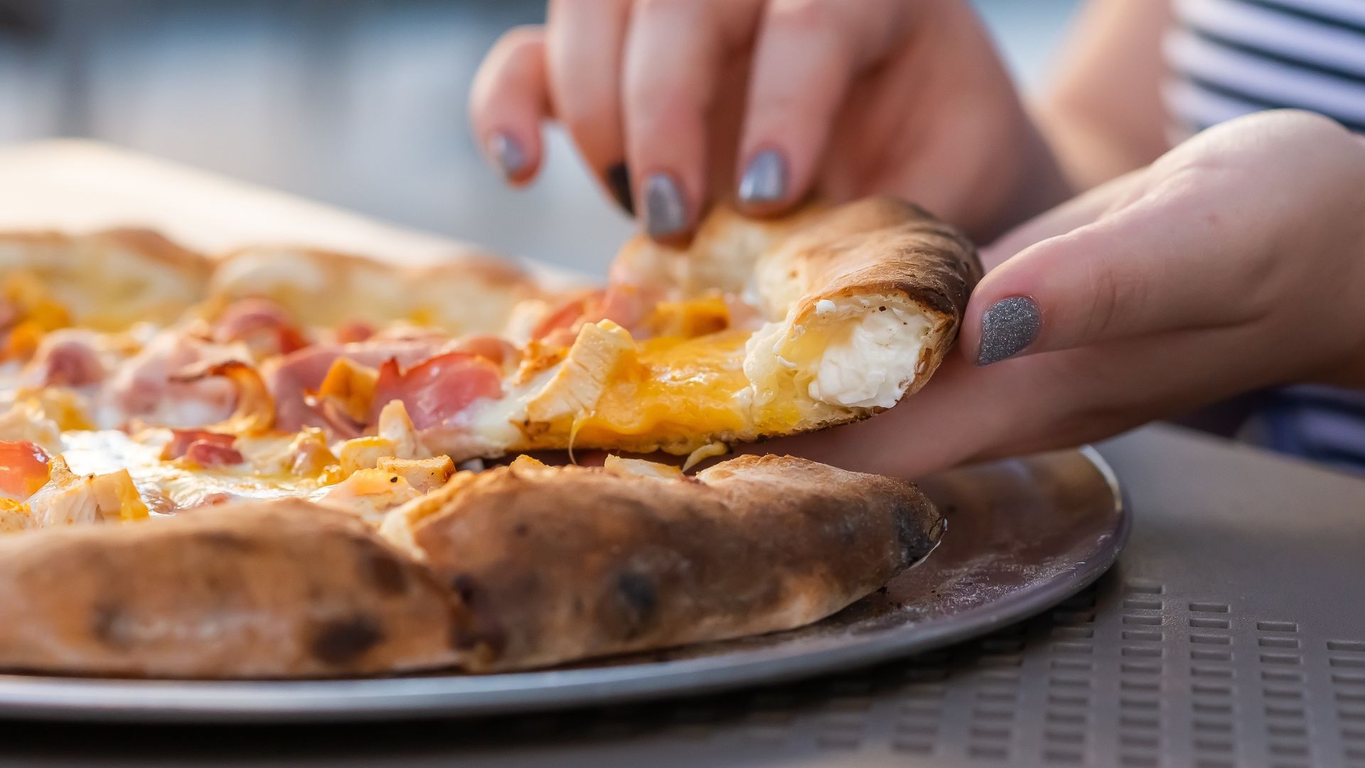 Hand lifting a slice of stuffed crust pizza with melted cheese visible inside the crust