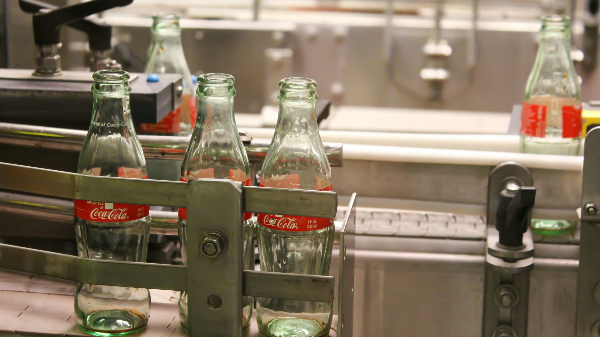 Glass Coca-Cola bottles moving along a conveyor belt in a beverage bottling facility.