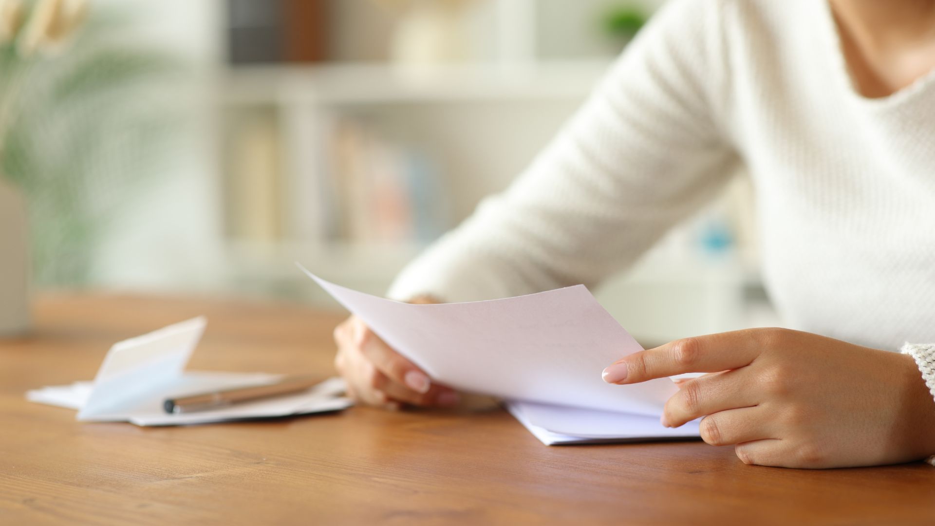 Person holding and reading a letter at a wooden table.
