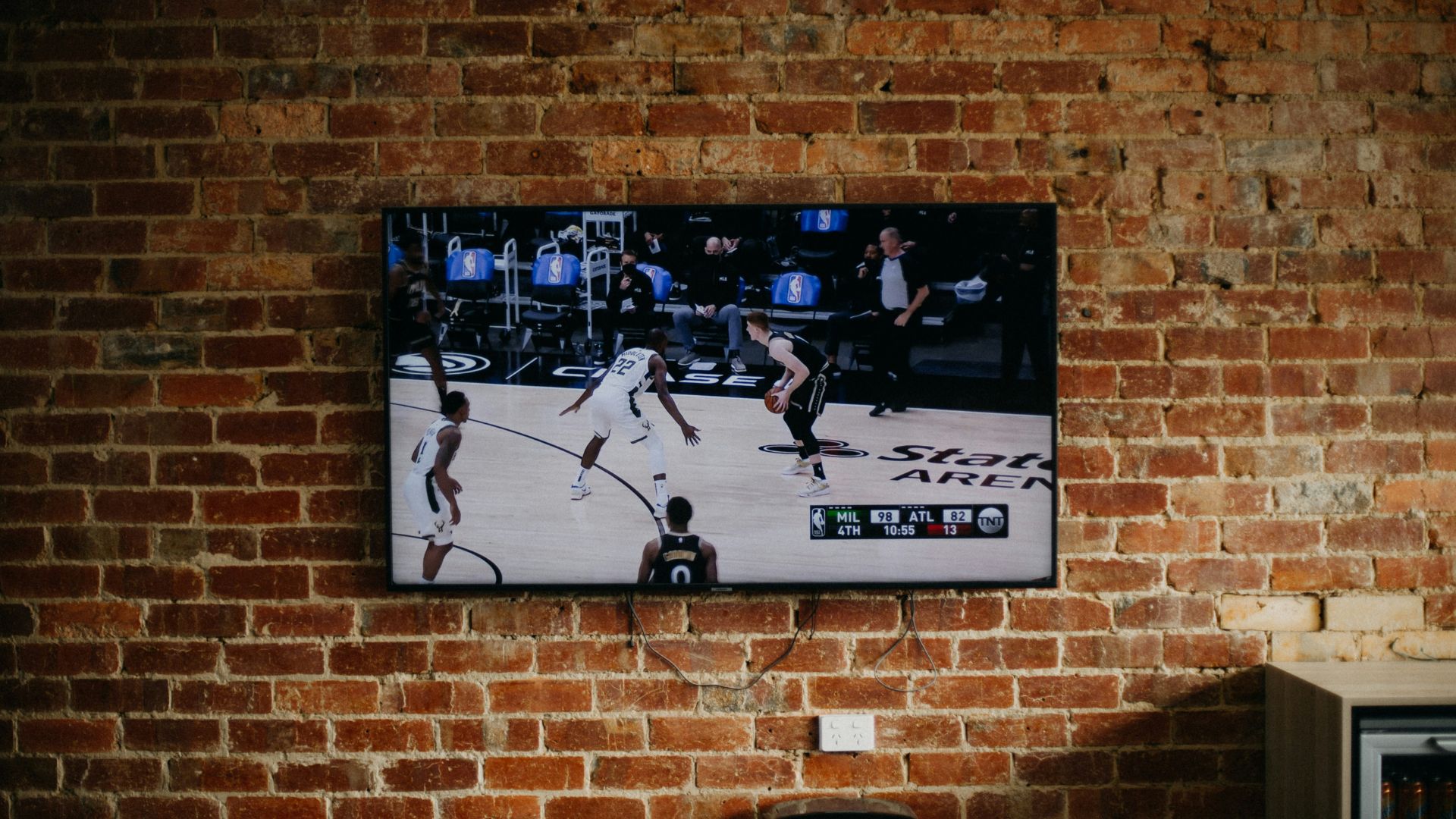 Television mounted on a brick wall displaying a live basketball game broadcast