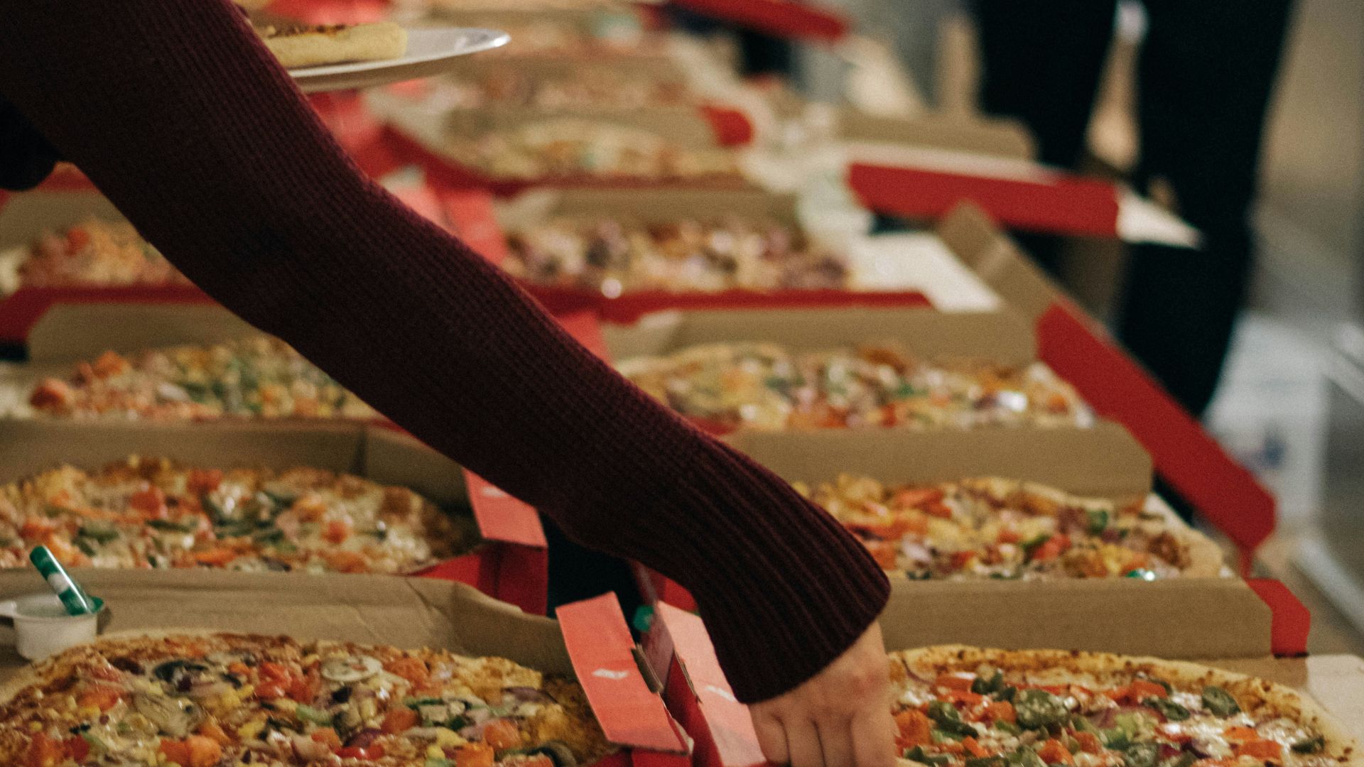 Person reaching across a table to grab a slice from a freshly served pizza