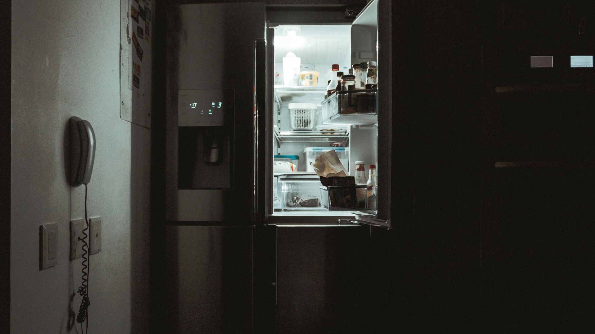 Open refrigerator at night showing shelves with food containers and condiments inside