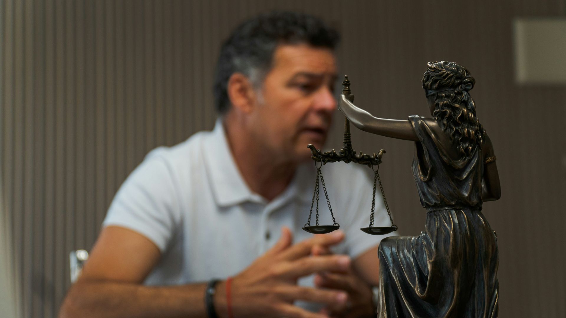 Statue of Lady Justice with scales in focus as a man speaks in the background during a legal consultation.