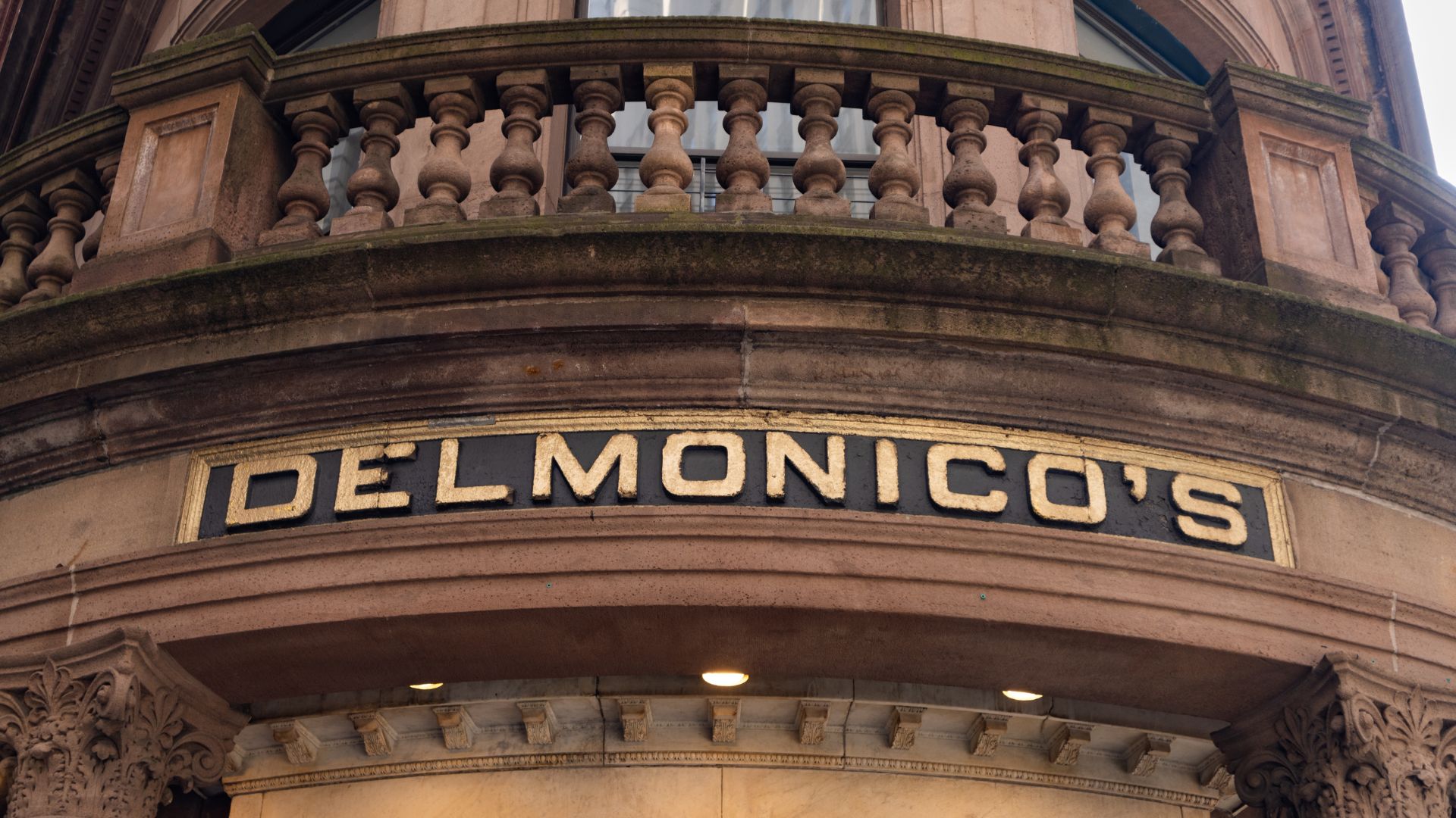 Delmonico’s restaurant sign on historic building facade with stone balcony above.