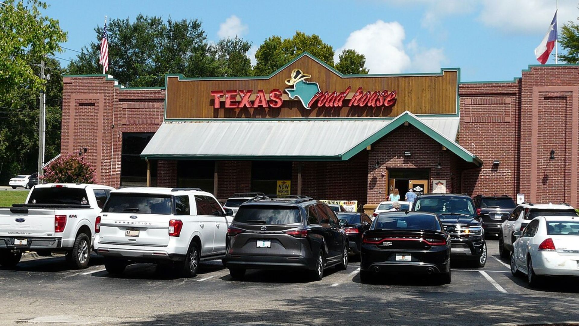 Exterior of Texas Roadhouse restaurant with parked cars outside and customers entering the building.