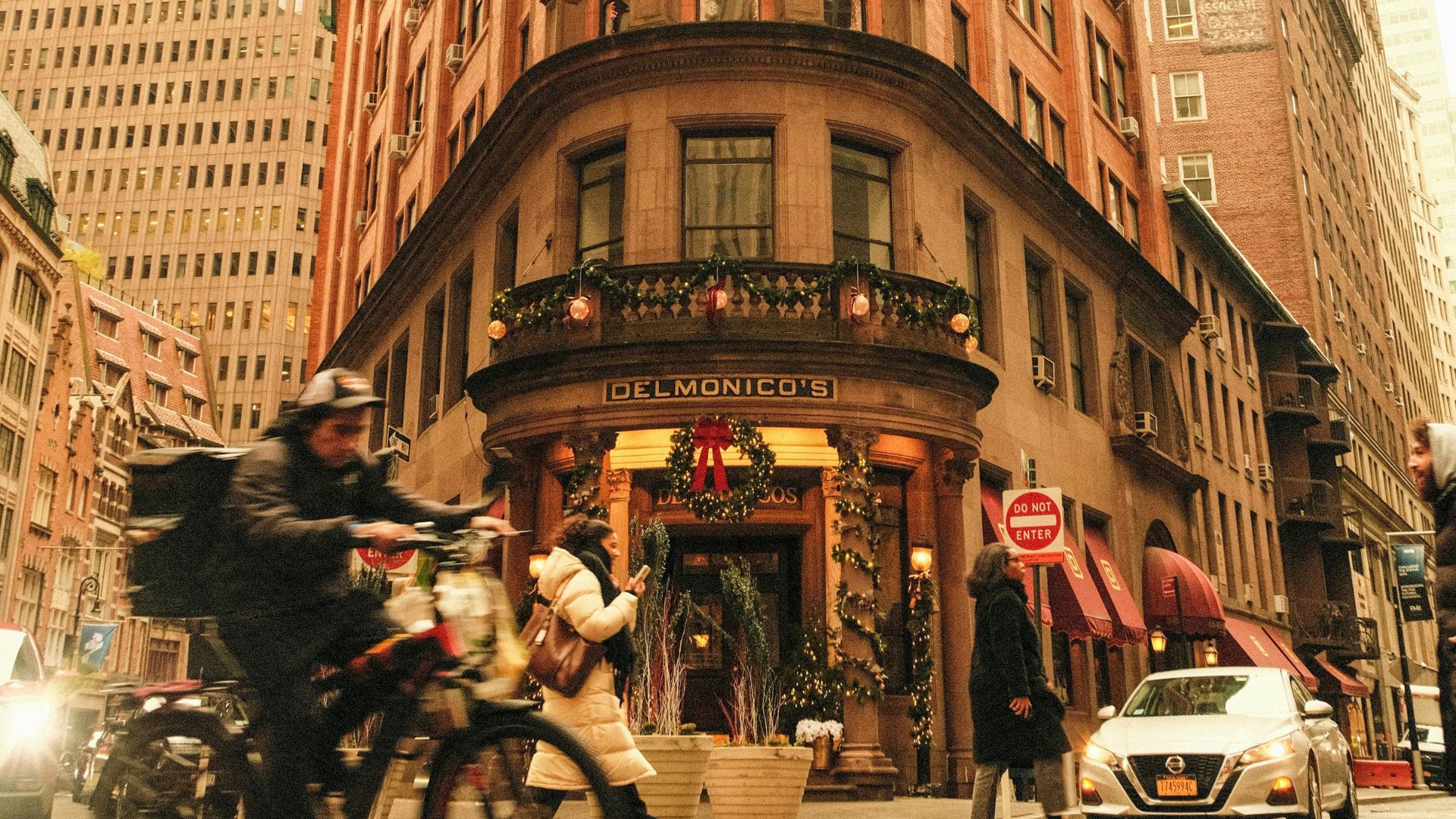Delmonico’s restaurant decorated for holidays with pedestrians and cyclist outside.