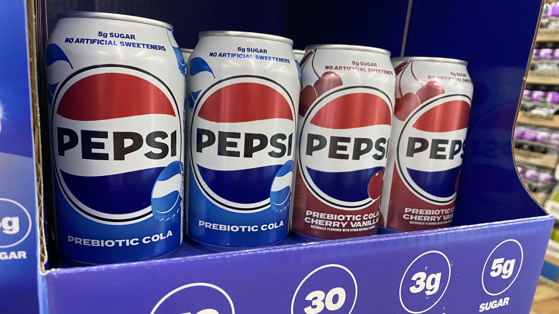 Pepsi prebiotic cola and cherry vanilla cans displayed on a retail store shelf.